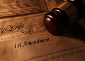 Papers reading "1st Amendment" and "We the People" are on a desk along with a gavel.