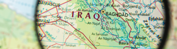 A magnifying glass above a map focuses on the country of Iraq