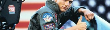 Tom Cruise as Maverick gives a thumbs up while sitting in an open fighter jet cockpit.