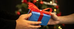 A closeup of a wrapped present being given with a christmas tree in the background.